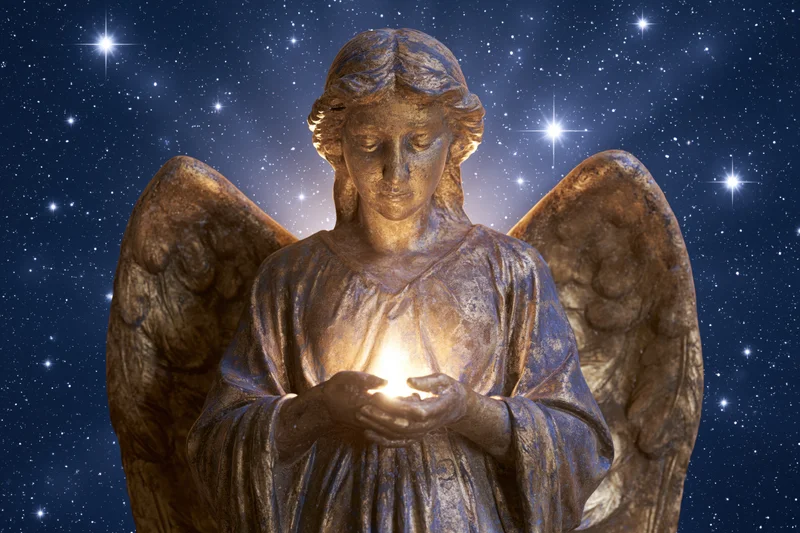 Golden stone angel statue with folded wings holding glowing light against starry night sky