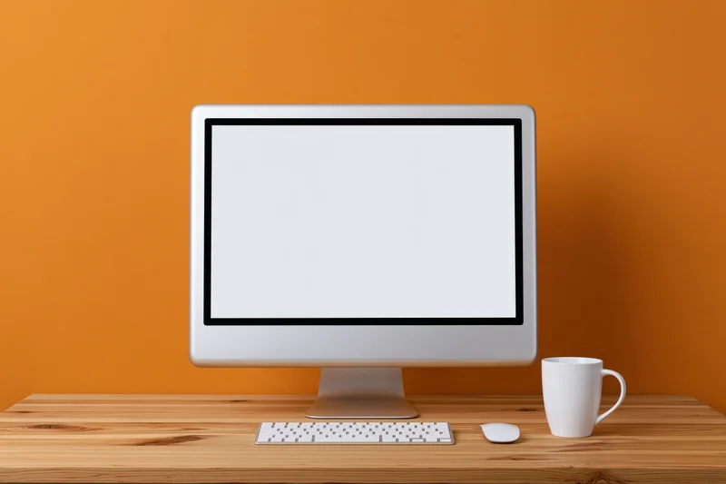 All-in-one desktop computer with blank white screen on wooden desk against orange wall
