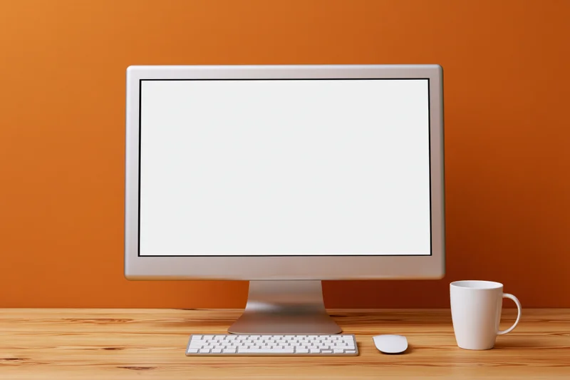 All-in-one desktop computer with blank white screen on wooden desk beside mug