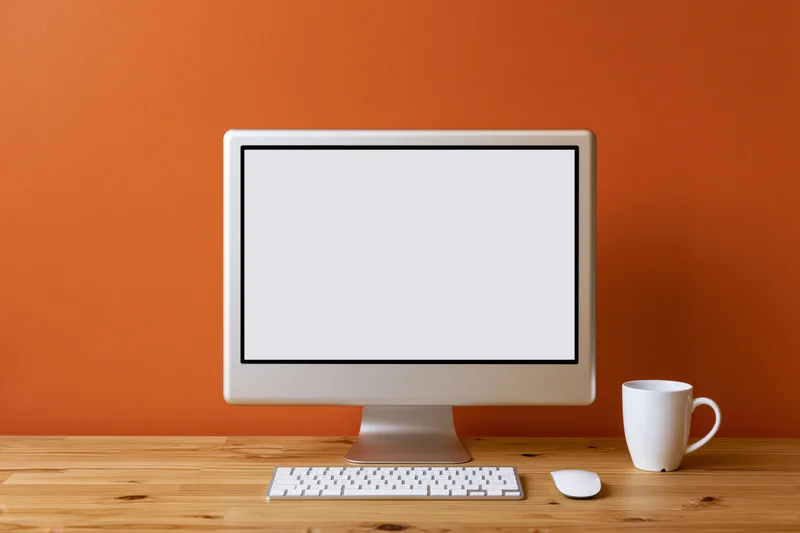 All-in-one desktop computer with blank white screen on wooden desk against orange wall