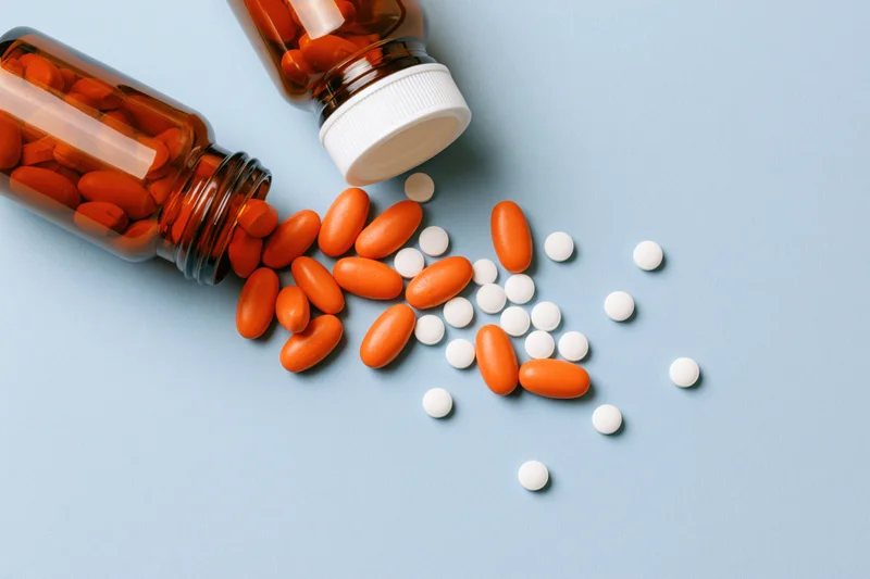 Amber glass medicine bottles lying on side with orange and white pills spilled onto blue surface