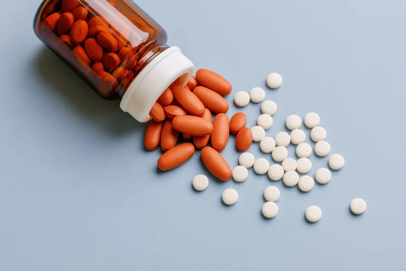 Amber glass bottle lying on its side with orange and white pills spilling onto a blue surface