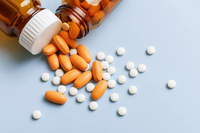 Amber glass medicine bottle lying on its side with orange and white pills spilled onto a blue surface