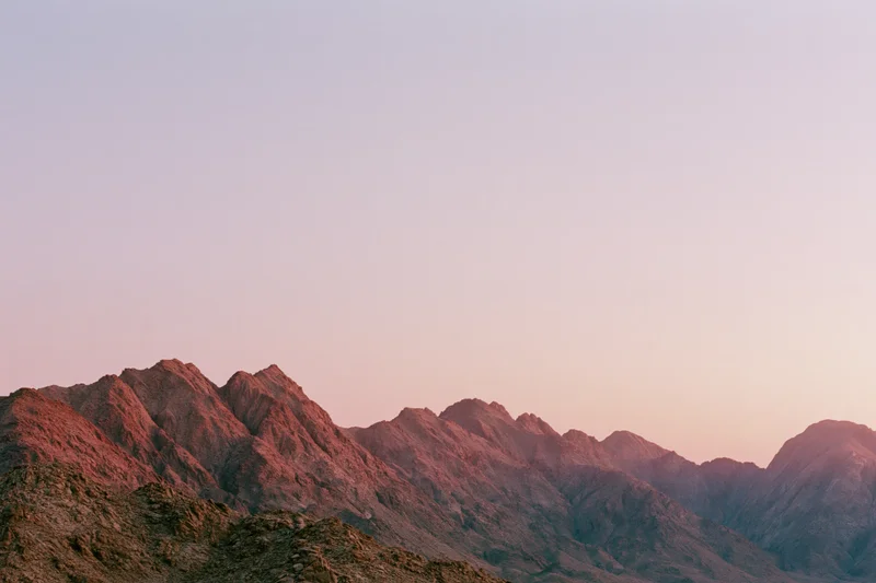 Jagged rocky mountain ridgeline at dusk under pastel sky