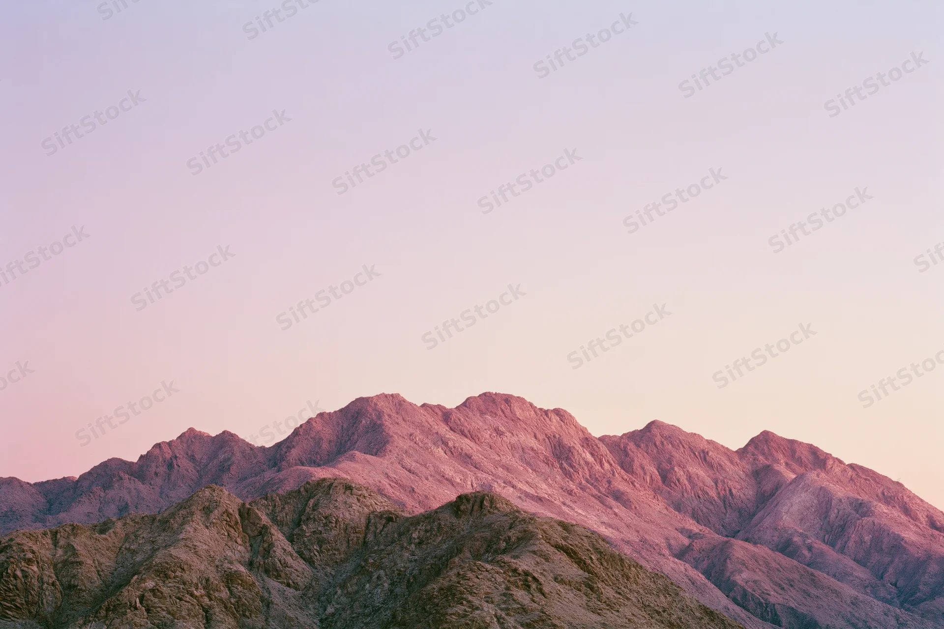 Arid mountain ridgeline at dusk with jagged rocky peaks under pastel sky