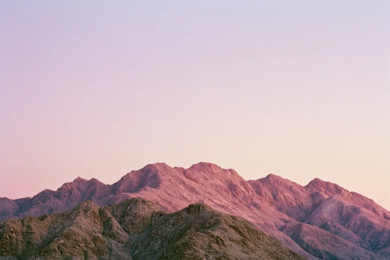 Arid mountain ridgeline at dusk with jagged rocky peaks under pastel sky