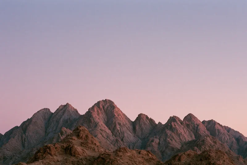 Jagged rocky mountain ridgeline at dusk under a pastel sky