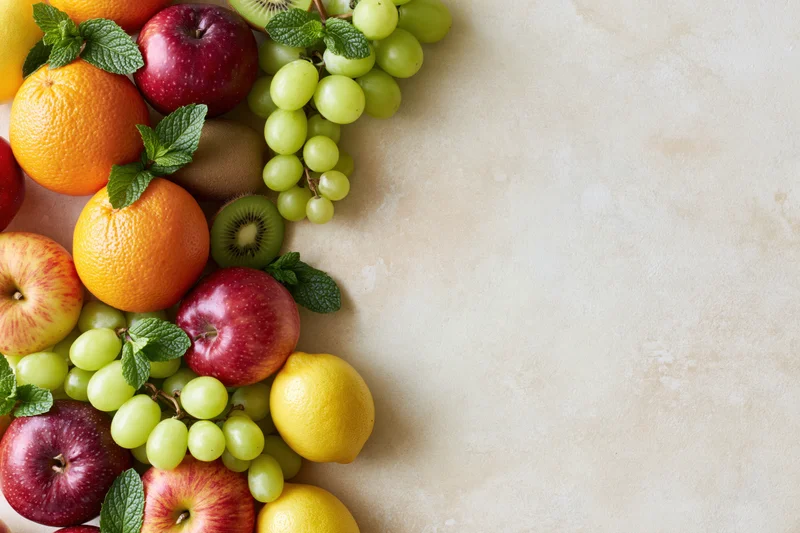 Assorted fresh fruits arranged in a border along the left side of a light beige surface