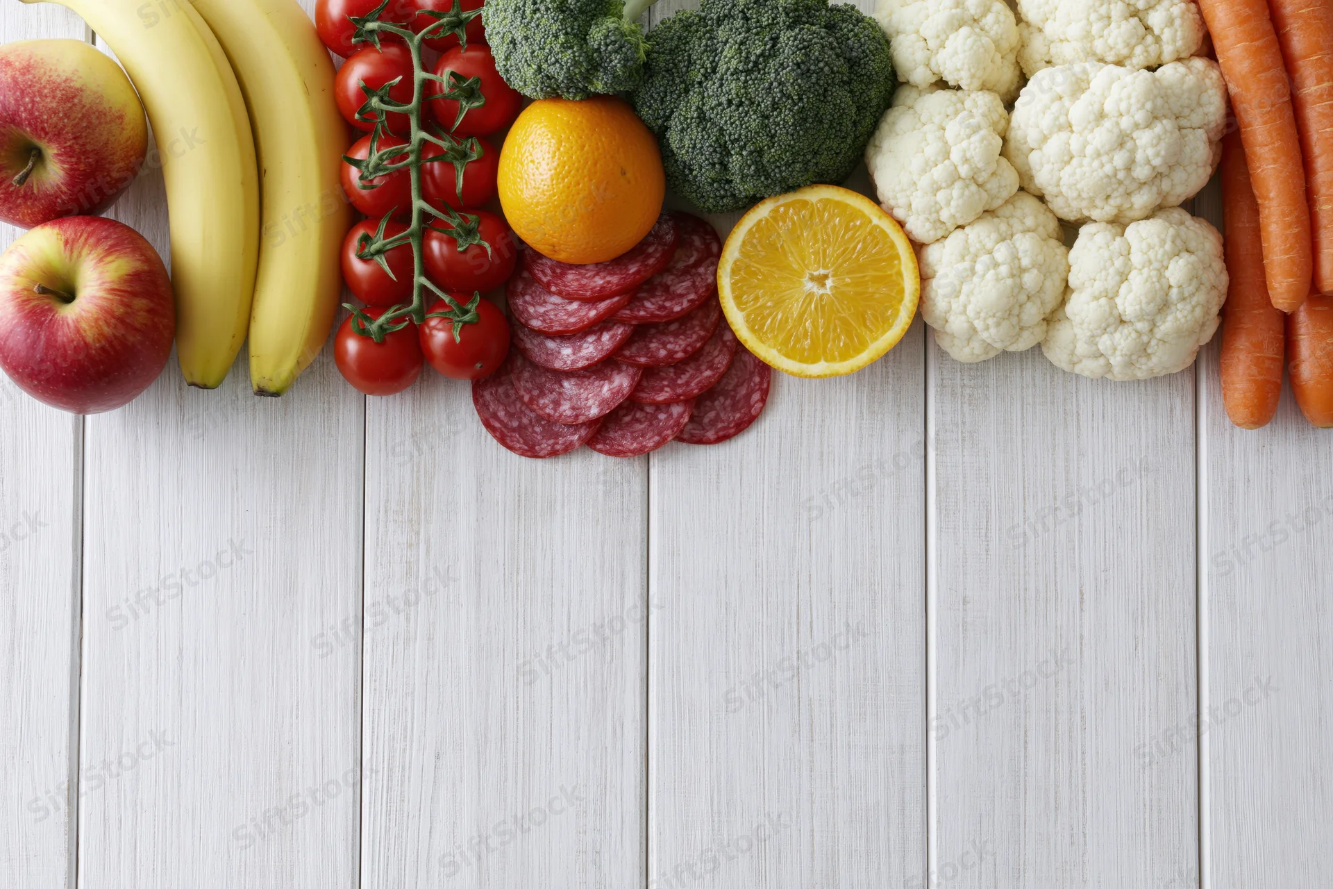 Assorted fresh fruits vegetables and sliced salami arranged on white wooden table in flat lay top view with copyspace
