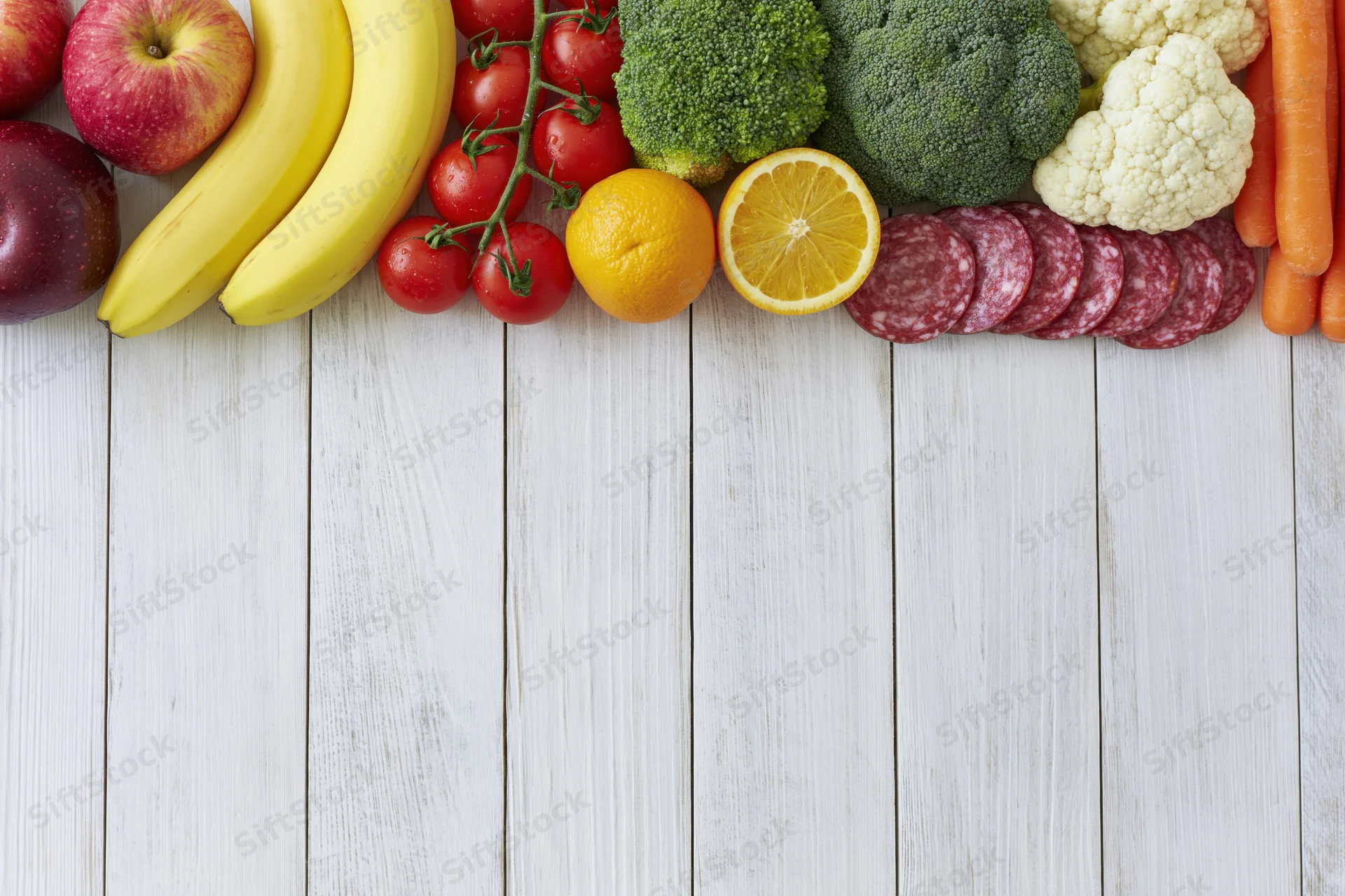 Assorted fresh fruits vegetables and sliced salami arranged on white wooden table in flat lay top view with copyspace below