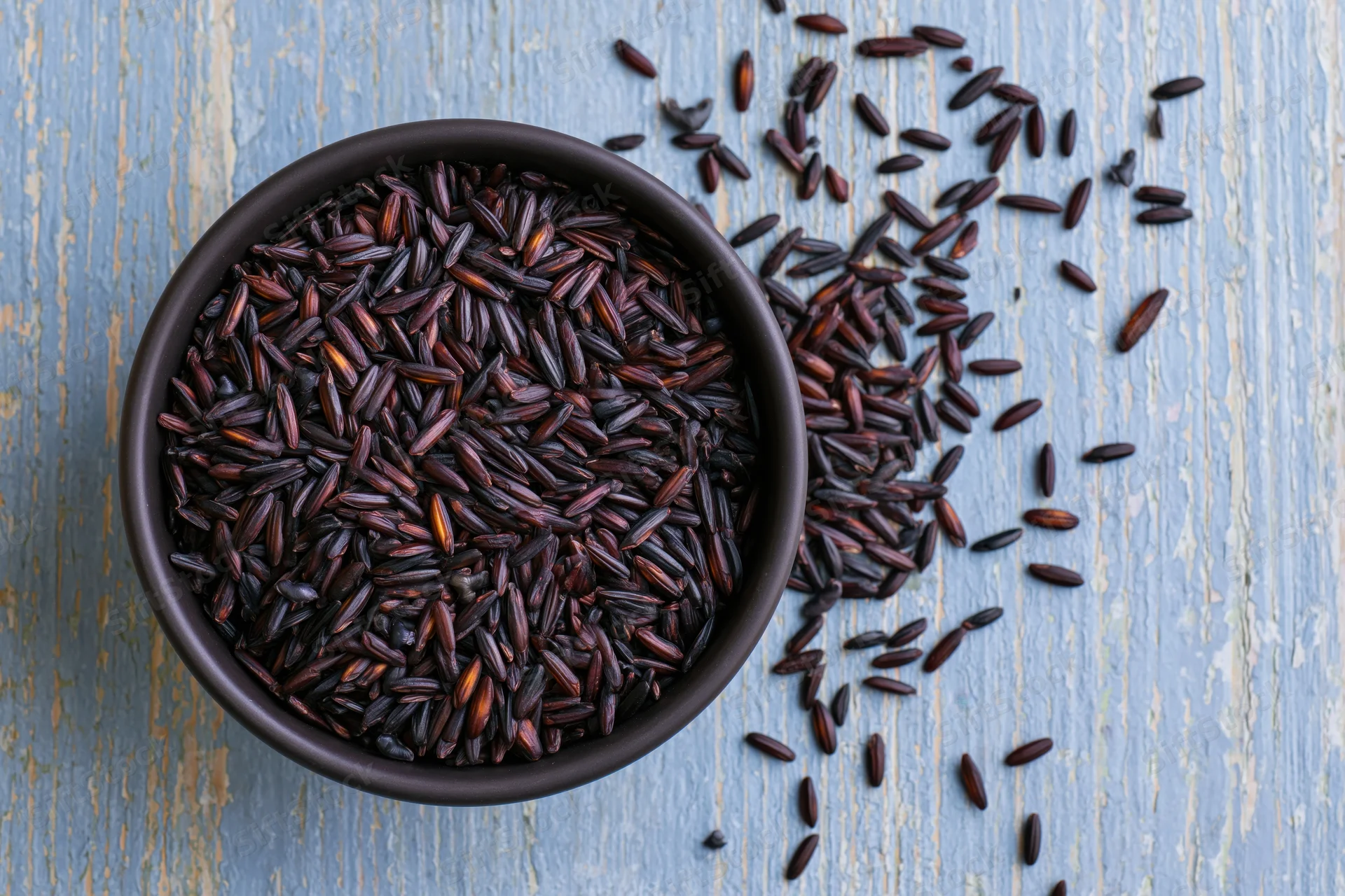 Black rice grains in a matte black ceramic bowl on a blue weathered wooden surface
