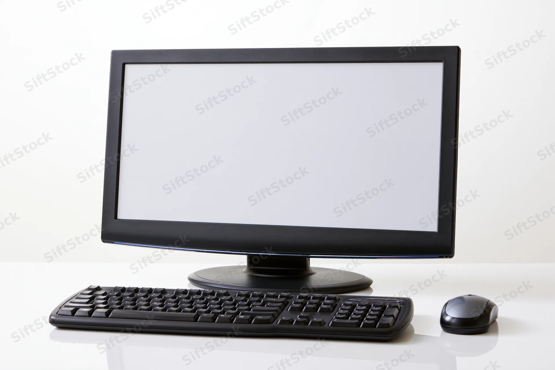 Black desktop computer monitor with blank white screen, keyboard and mouse on white surface