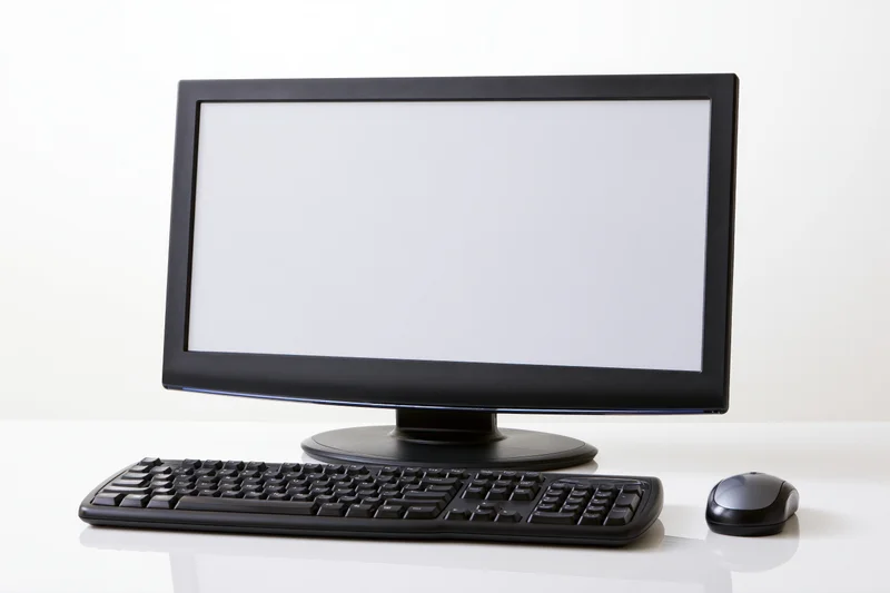 Black desktop computer monitor with blank white screen, keyboard and mouse on white surface
