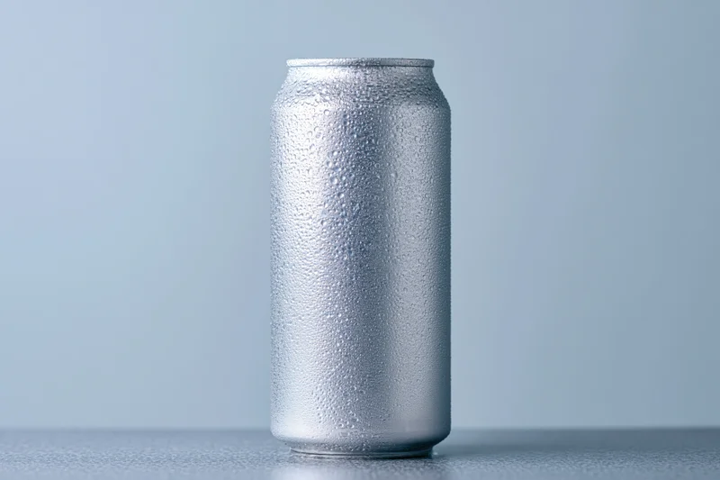 Aluminum beverage can covered in condensation droplets on a plain surface