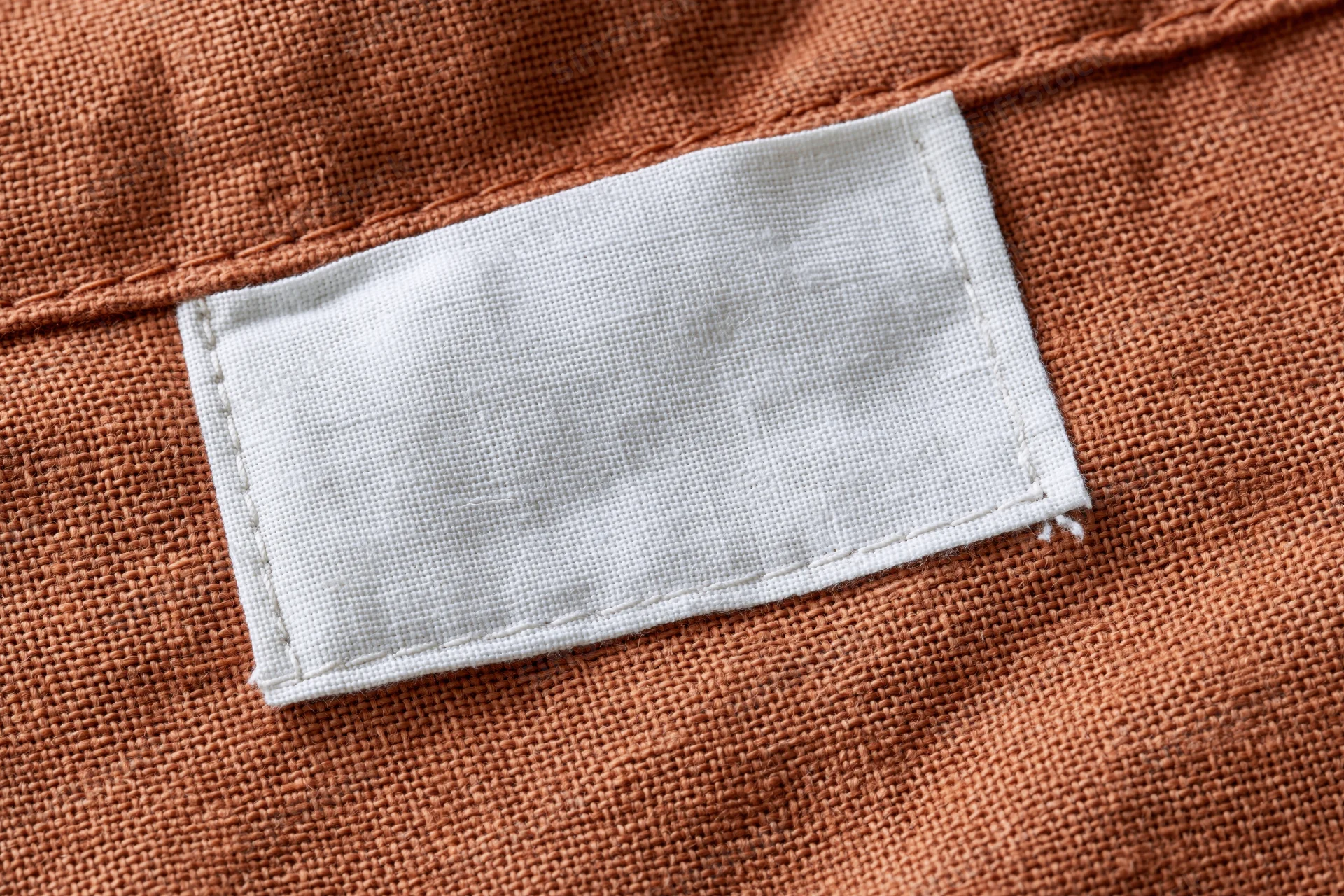 Blank white fabric label sewn onto orange textile garment interior
