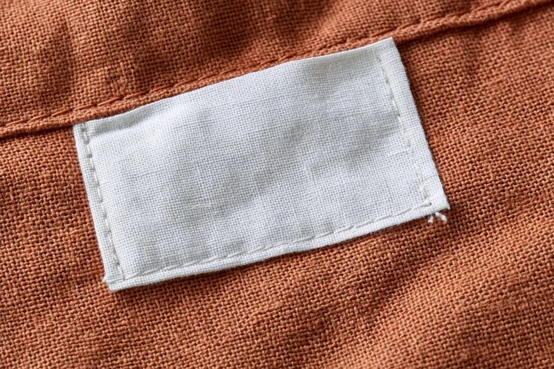 Blank white fabric label sewn onto orange textile garment interior