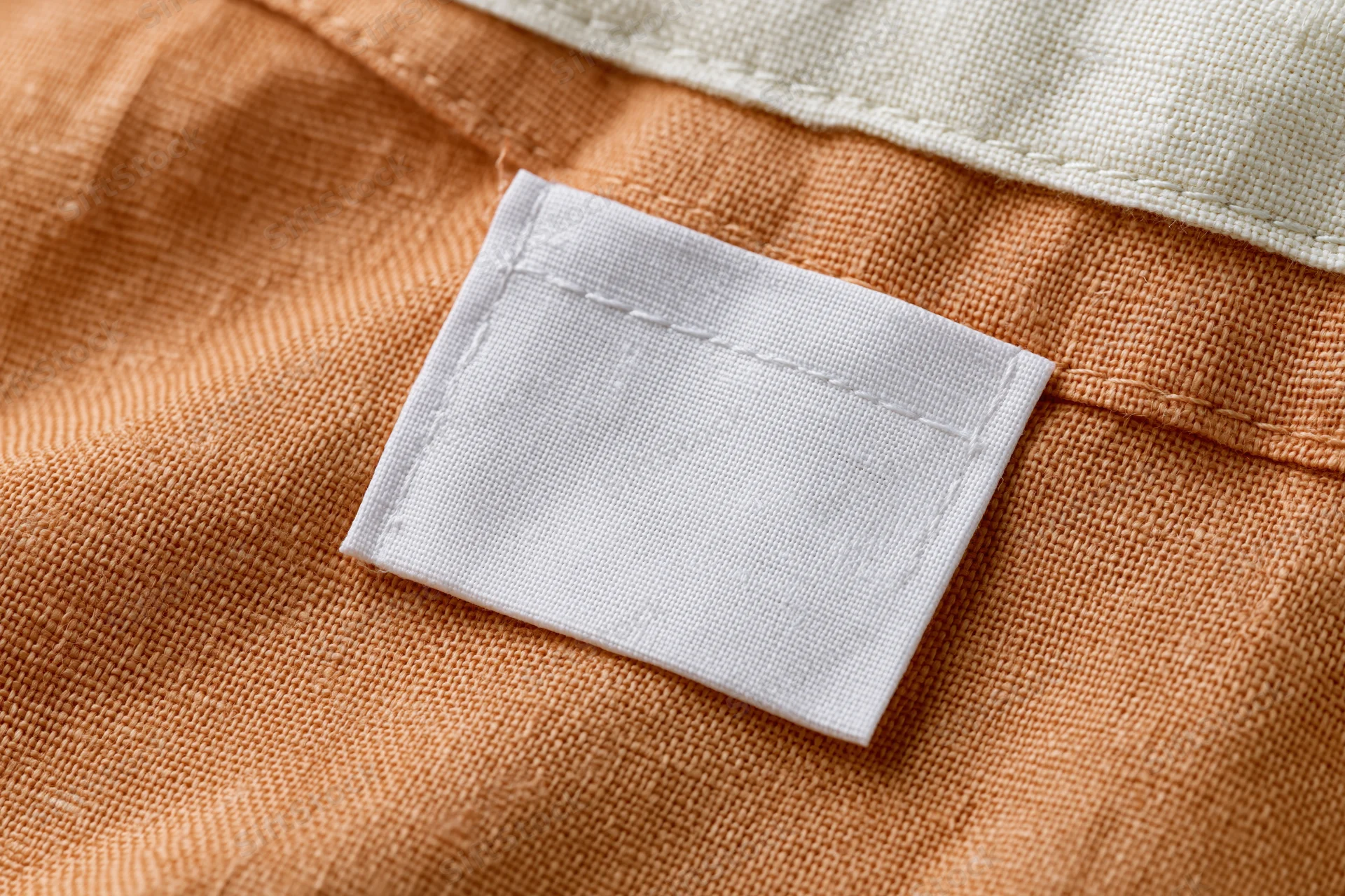 Blank white clothing label sewn onto orange fabric interior of garment
