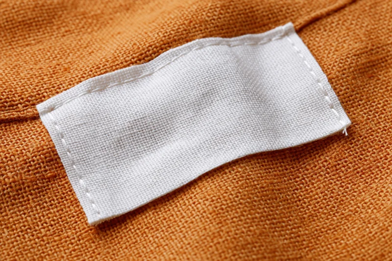 White fabric label sewn onto orange knit garment interior