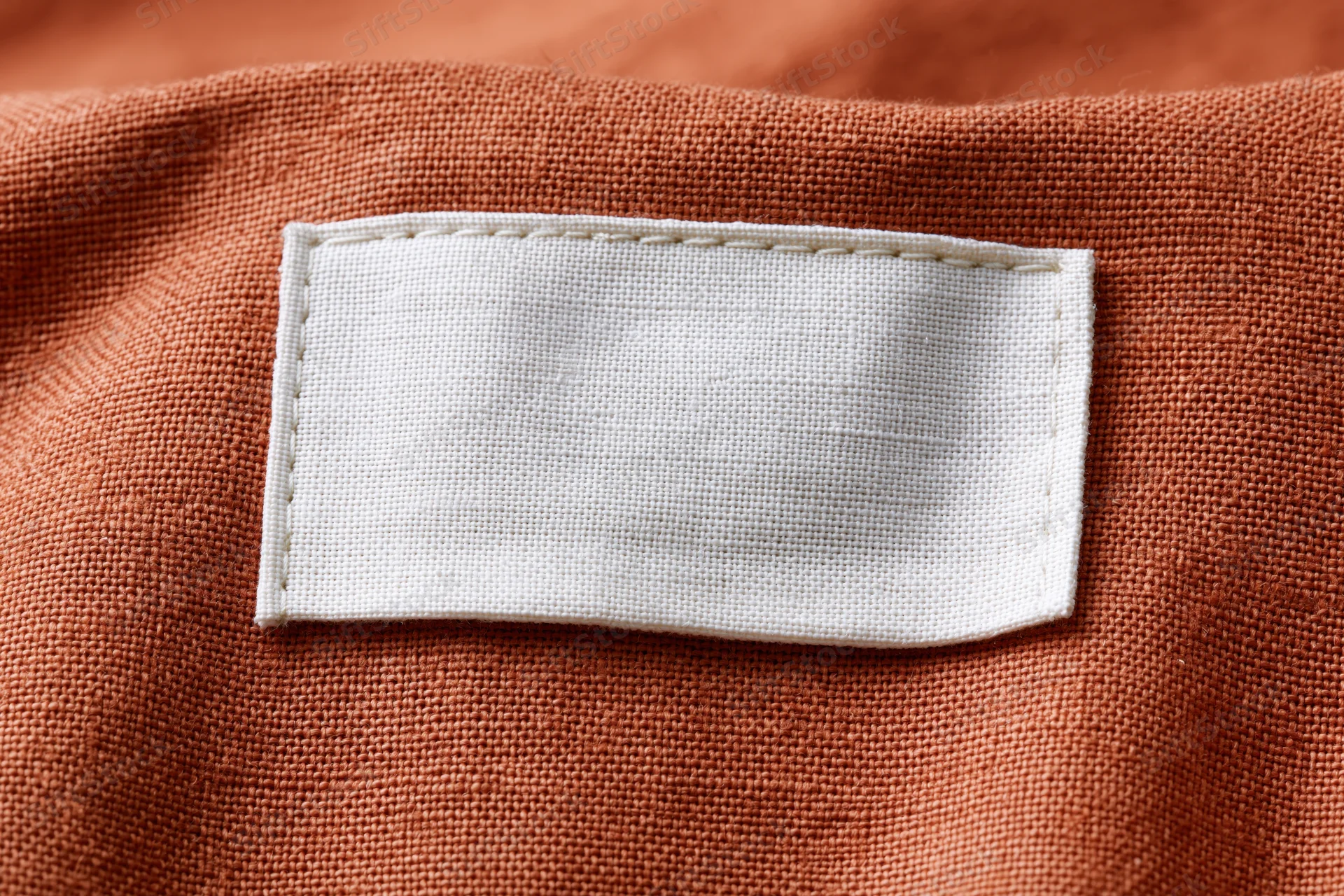 Blank white fabric label sewn onto orange garment interior