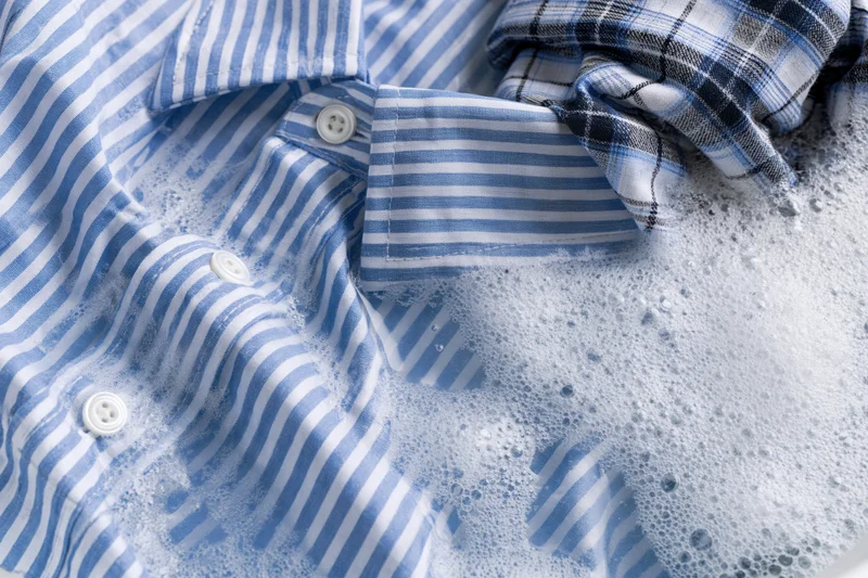 Blue and white striped shirt submerged in soapy water with foam and bubbles during washing
