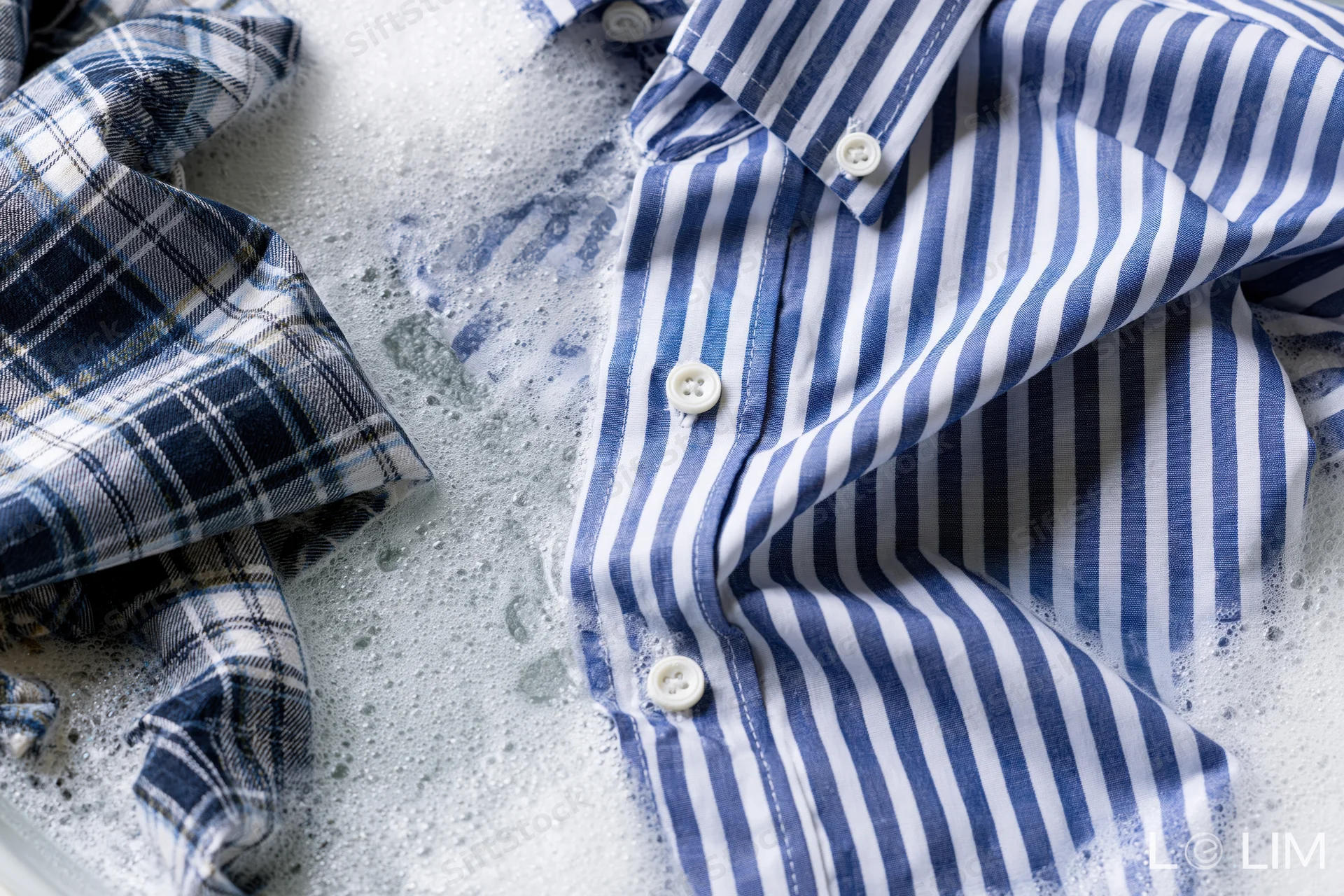 Blue and white striped shirt with buttons submerged in soapy water during washing
