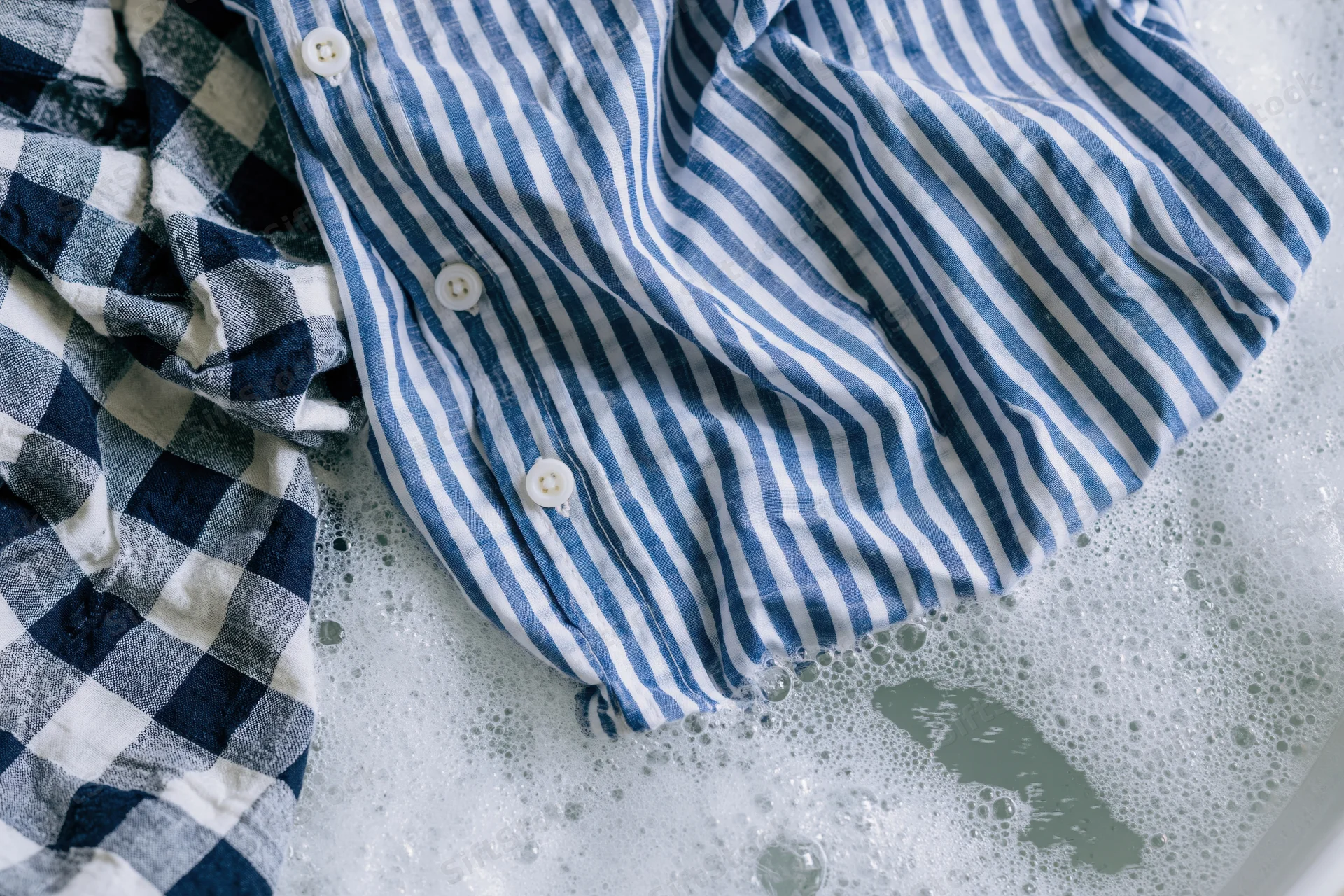 Blue and white striped shirt with buttons soaking in soapy water during laundry
