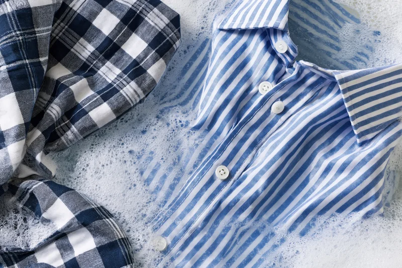 Blue and white striped shirt with buttons submerged in soapy water during laundry process