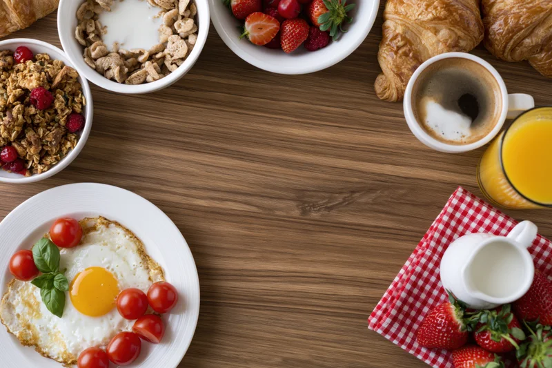 Breakfast spread arranged around empty wooden table center with copyspace