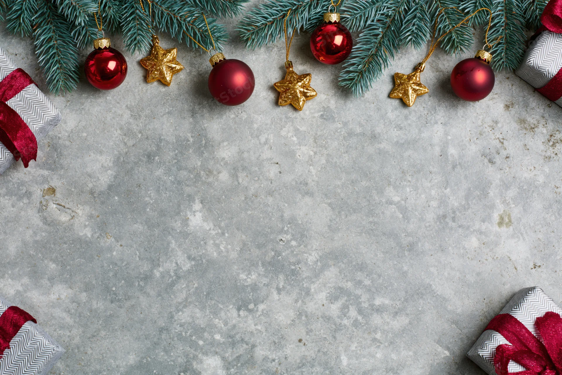 Christmas decorations and gifts arranged along the top and sides of a weathered grey concrete surface with copyspace in the center