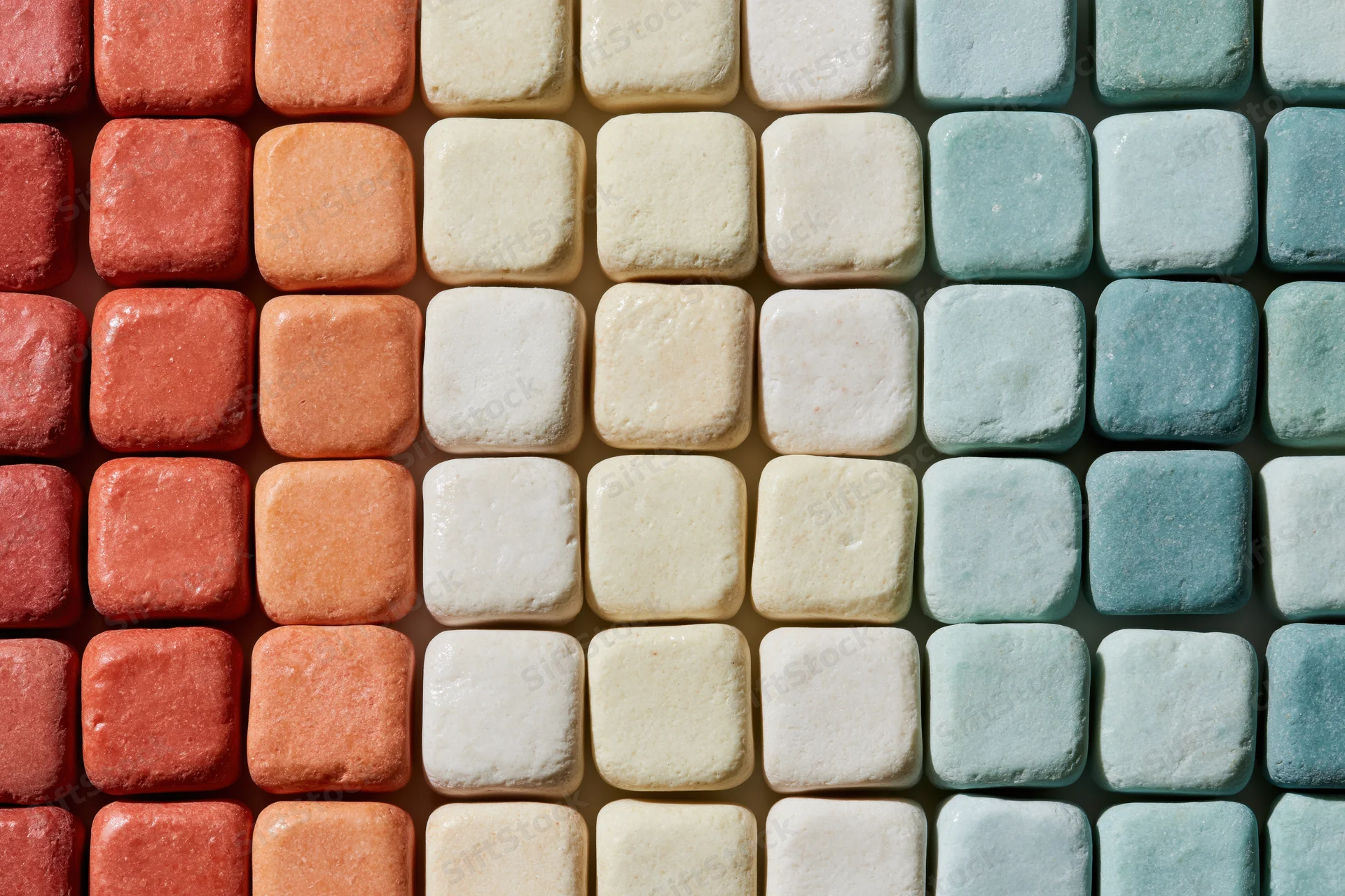 Grid of small rounded square ceramic tiles arranged in rows of red, orange, beige, white and blue hues in a flat lay overhead view