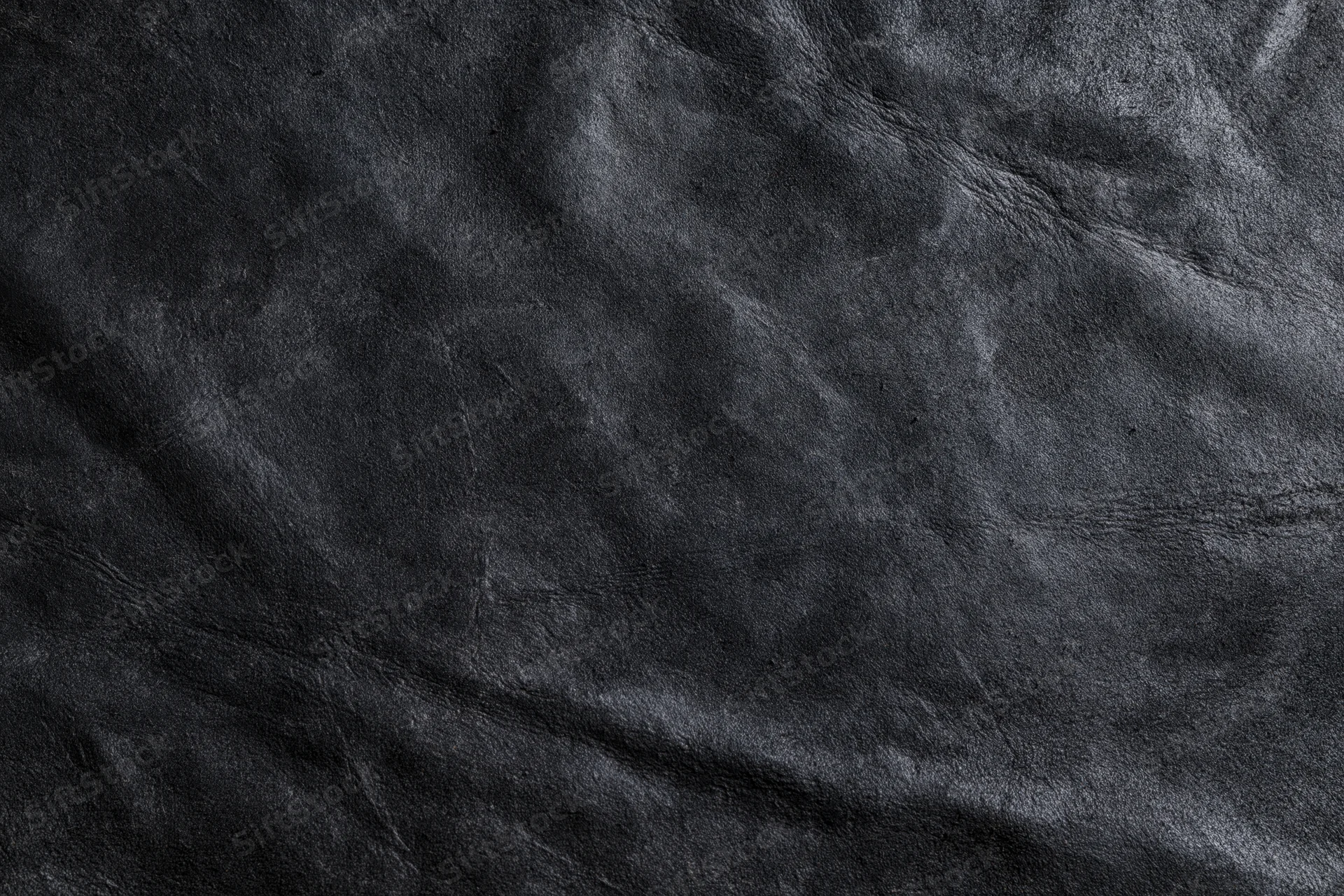 Close-up of dark black suede or matte leather surface with visible texture and wrinkles