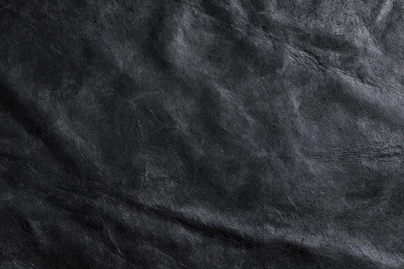 Close-up of dark black suede or matte leather surface with visible texture and wrinkles