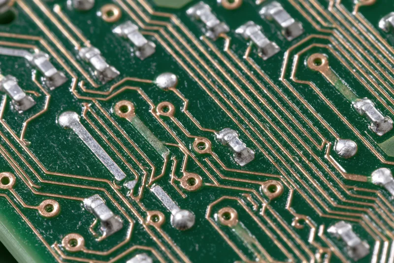 Close-up of a green printed circuit board with copper traces and soldered components