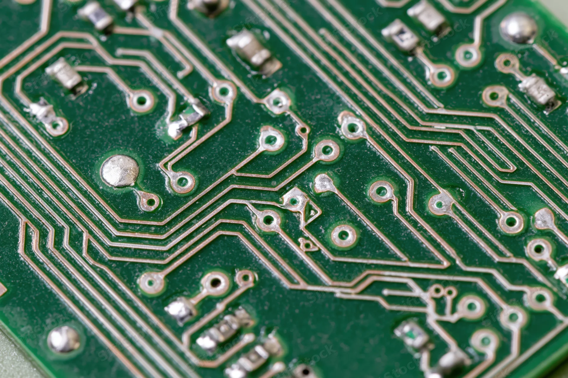 Close-up of a green printed circuit board with copper traces and soldered components