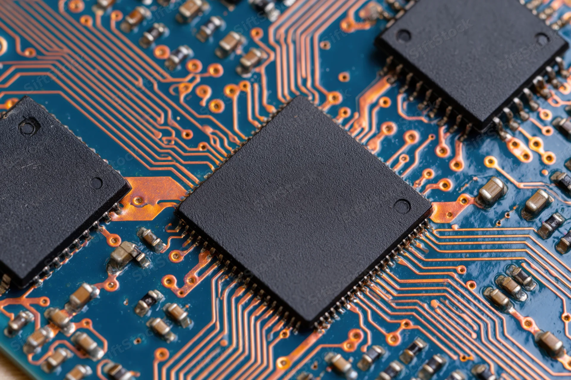Close-up of black microchips mounted on a blue circuit board with copper traces and surface-mount components