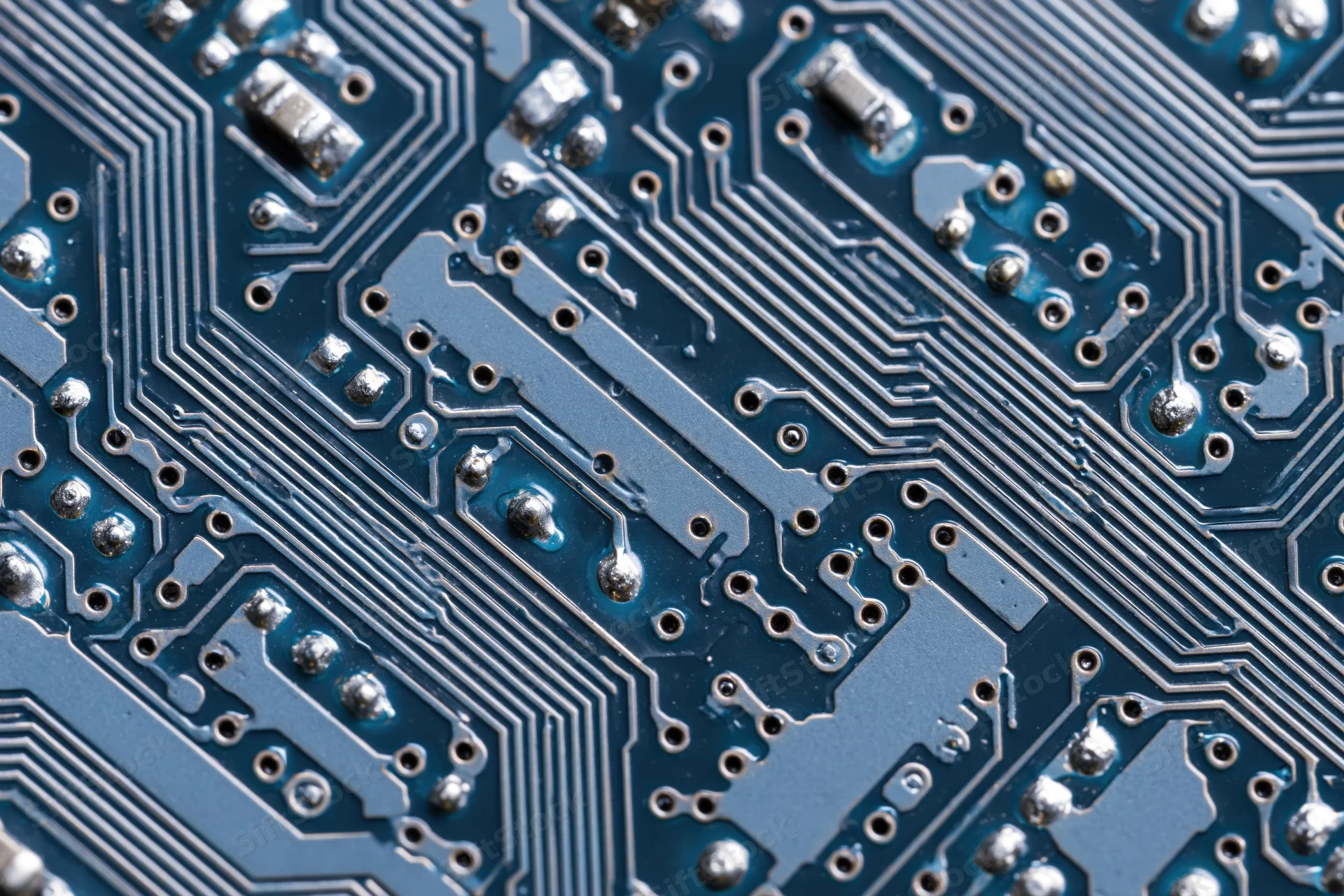 Close-up of a blue printed circuit board surface with silver traces and soldered components