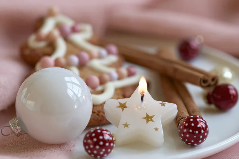 Gingerbread cookie with white star candle and red ornaments on a plate with cinnamon sticks and pink fabric