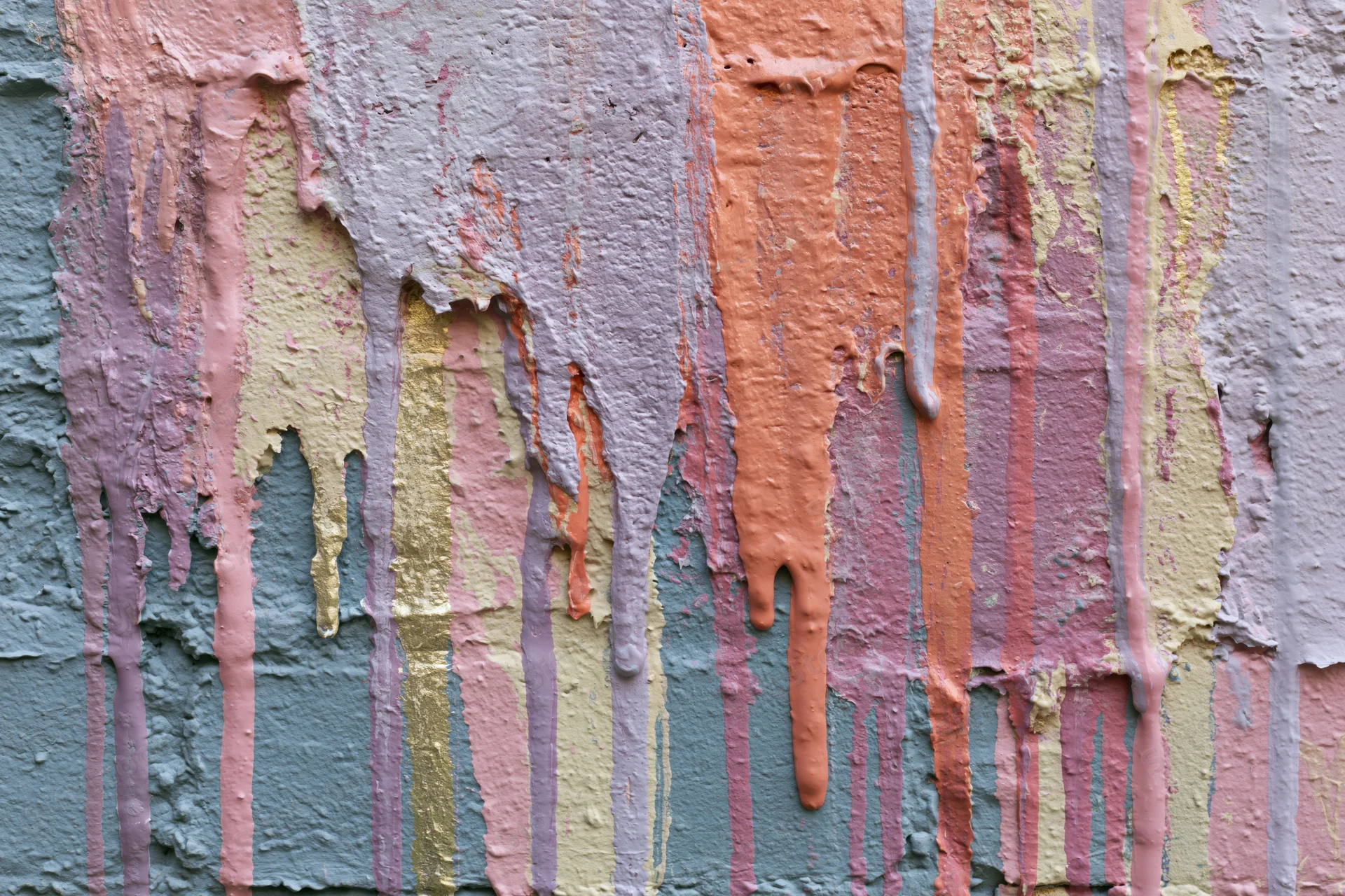 Close-up of a weathered wall with layers of peeling paint dripping vertically in pastel colors