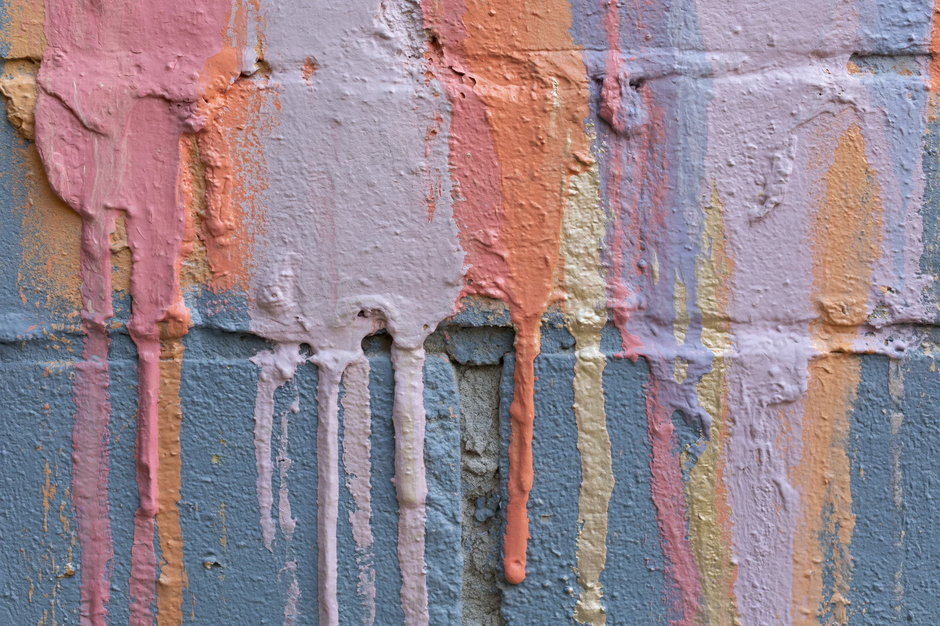 Close-up of paint drips on a textured concrete wall with layered pastel colors