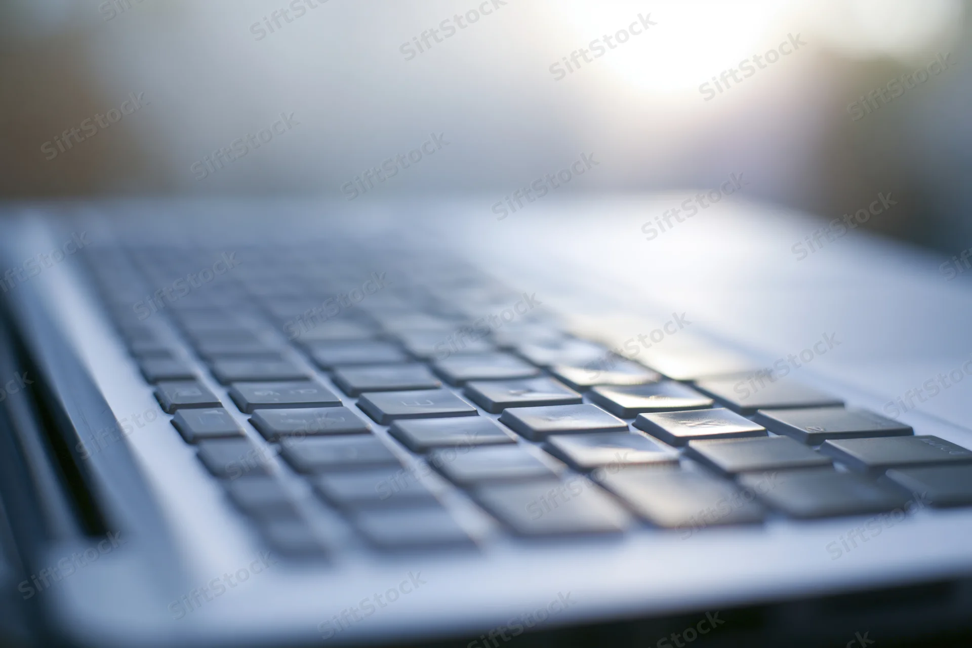 Close-up of laptop keyboard from low side angle with sunlight flare on keys