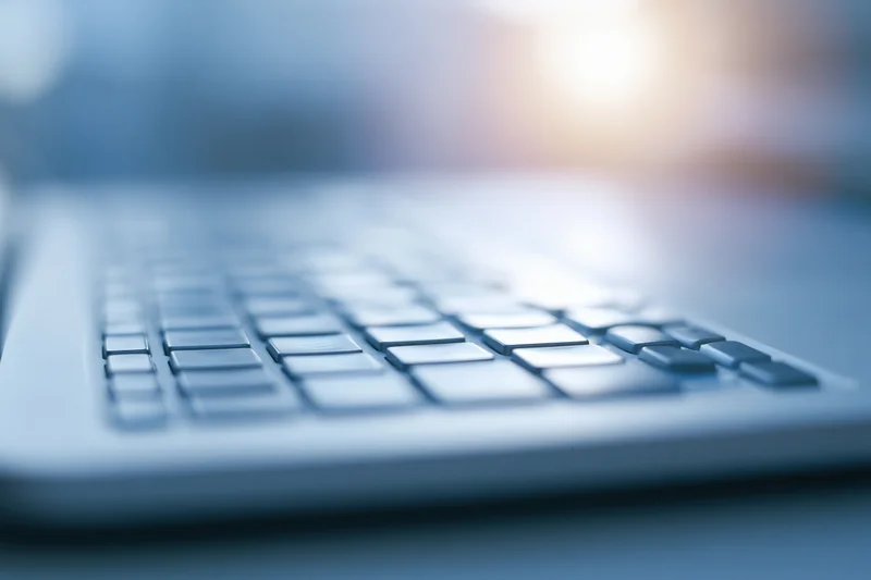 Close-up of laptop keyboard from low side angle with shallow depth of field and soft light reflection