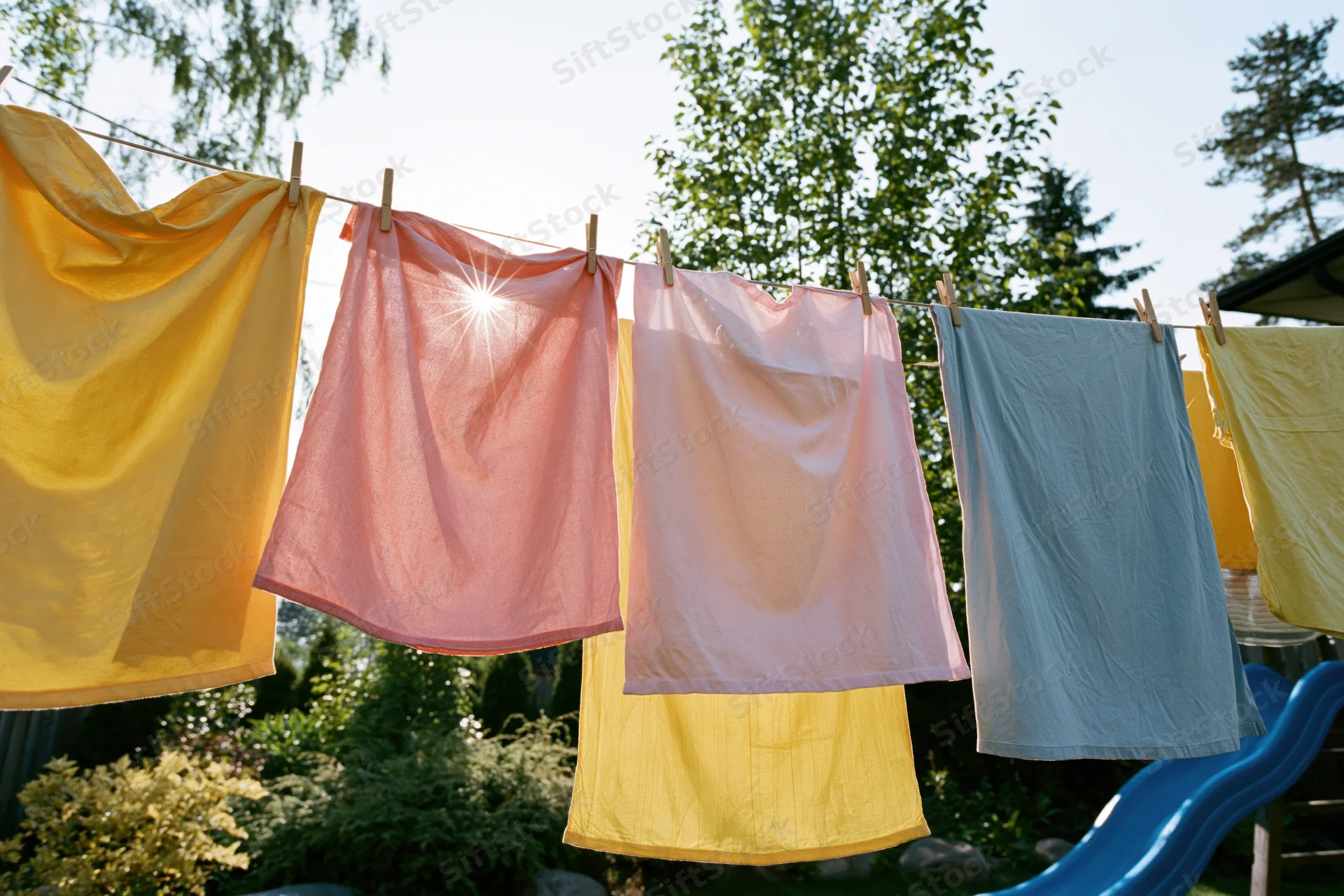 Colorful laundry drying on a washing line in a backyard garden with sunlight filtering through the fabric