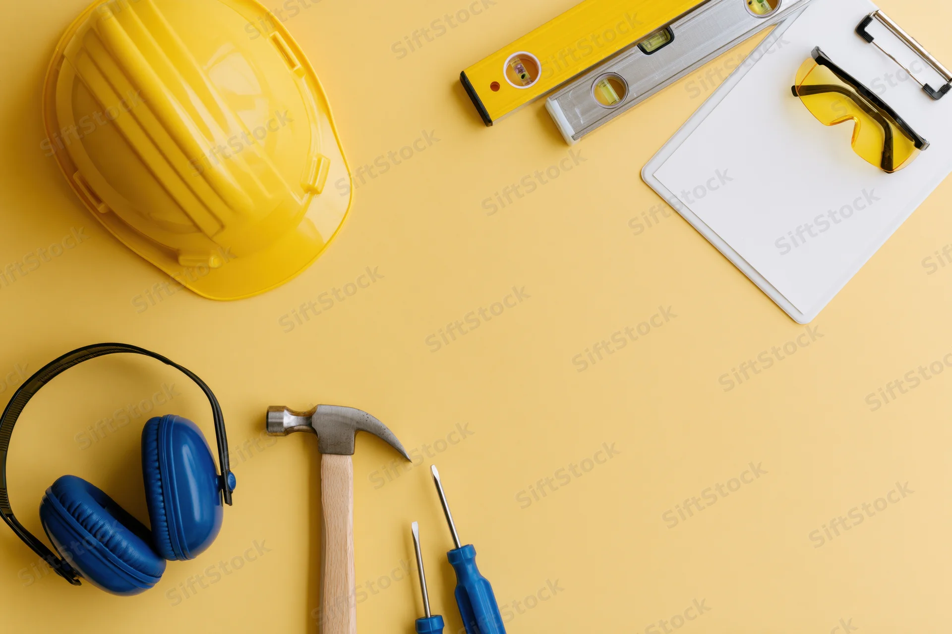 Construction safety equipment and hand tools arranged on a yellow surface with copyspace