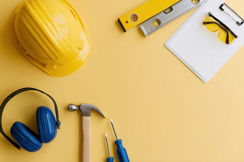 Construction safety equipment and hand tools arranged on a yellow surface with copyspace
