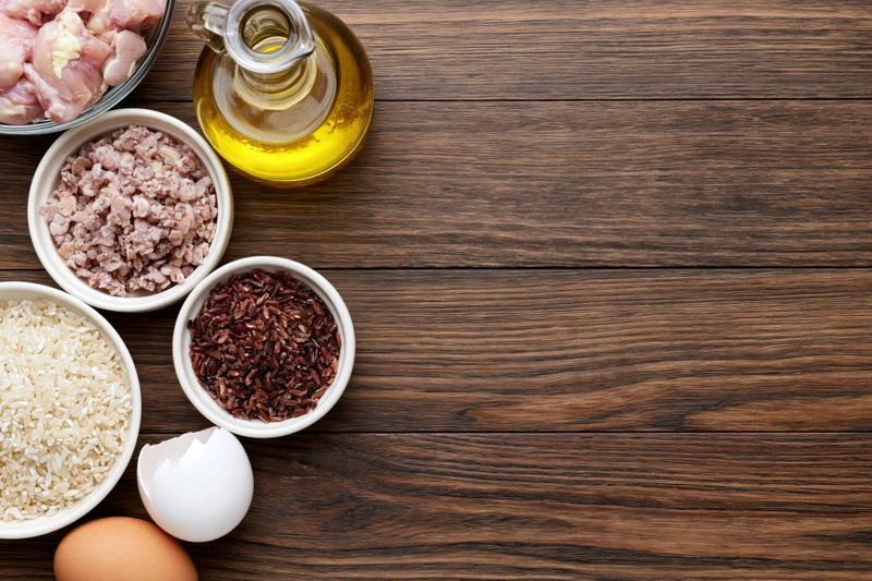 Cooking ingredients arranged in bowls and a bottle on a dark wooden table top view