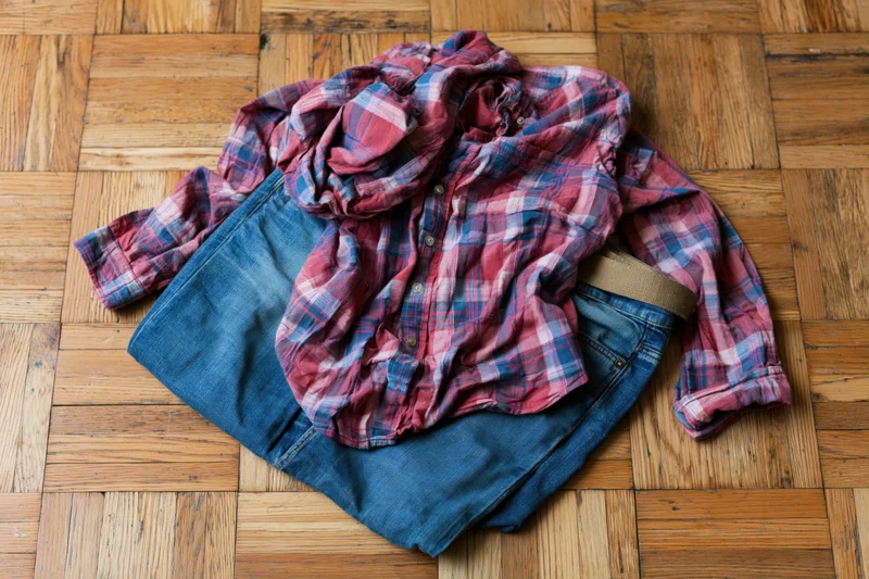 Crumpled red plaid flannel shirt on folded blue jeans on wooden parquet floor