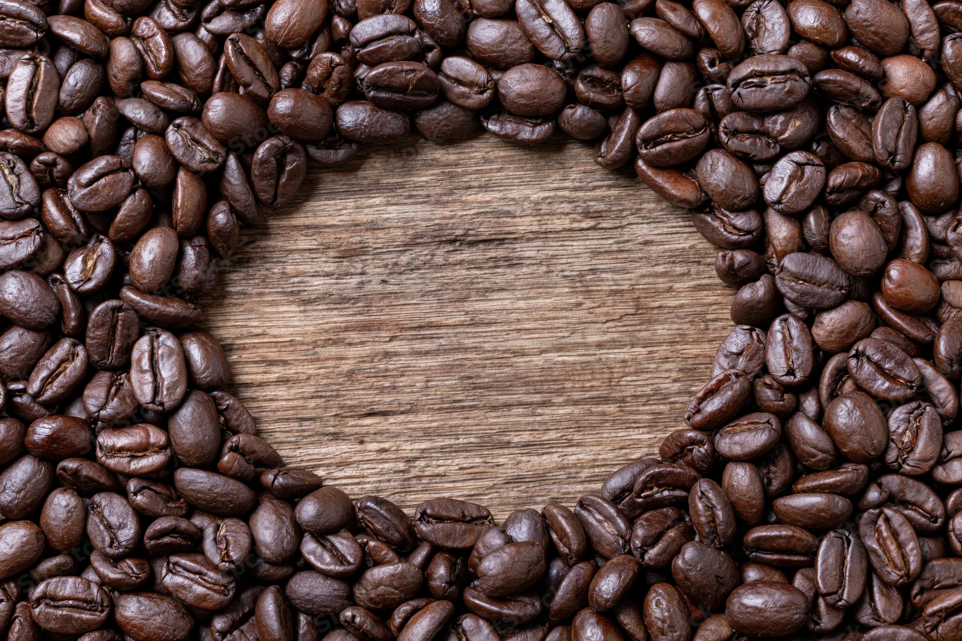 Dark roasted coffee beans arranged in heart shape on wooden surface with central copyspace