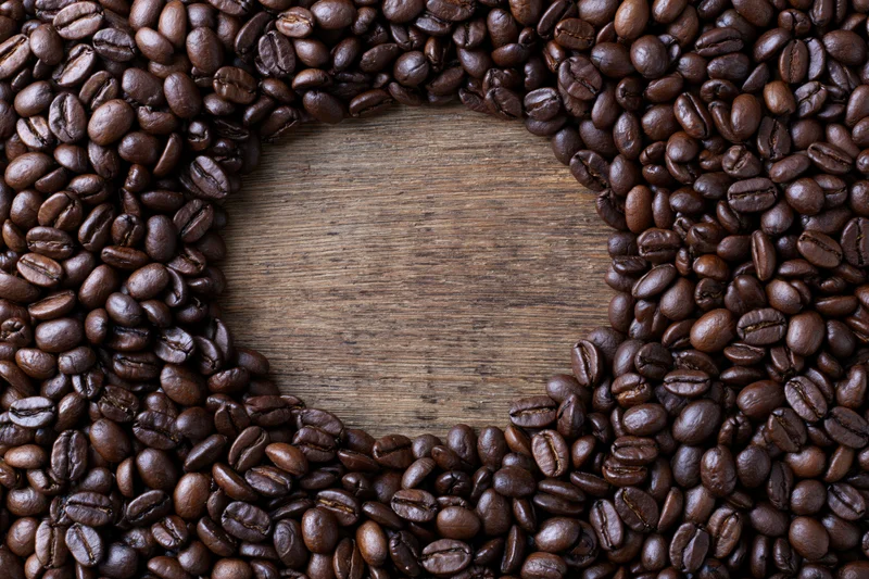 Coffee beans arranged in a border around a wooden surface with central copyspace