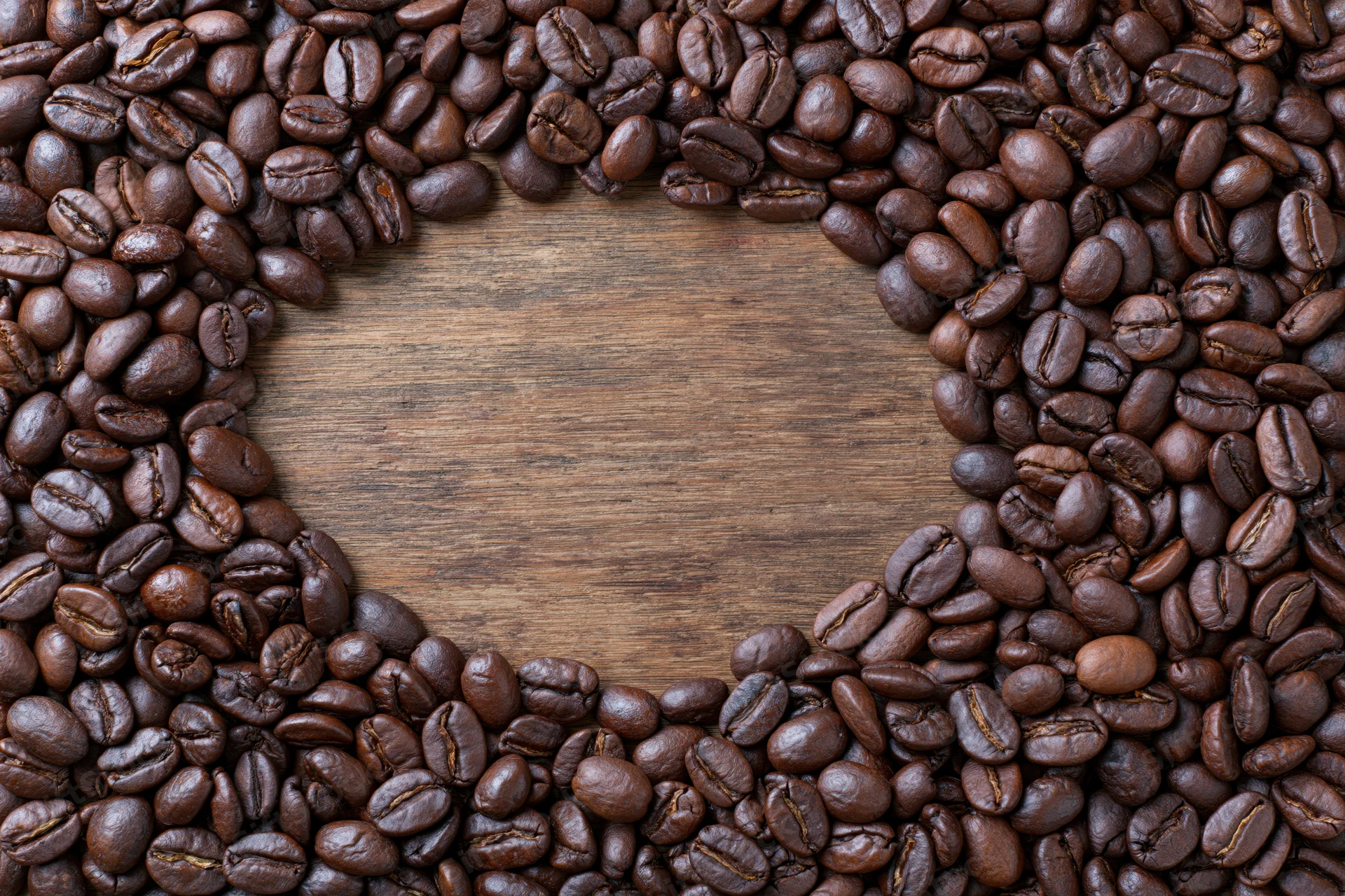 Dark roasted coffee beans arranged in heart shape on wooden surface with central copyspace