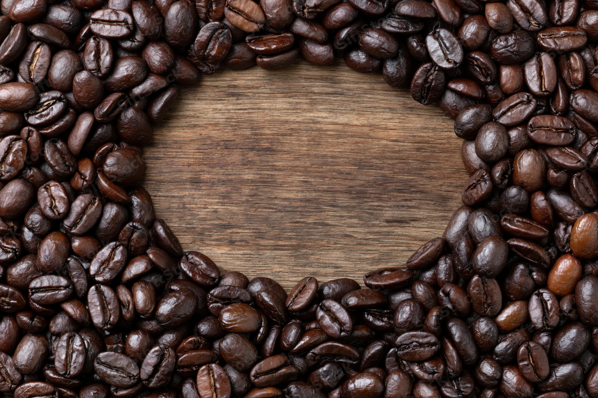 Dark roasted coffee beans arranged in heart shape on wooden surface